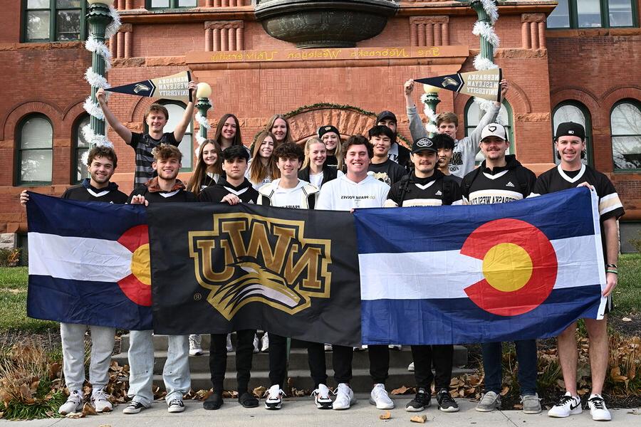 A group of students from Colorado hold up two Colorado flags and one NWU flag.